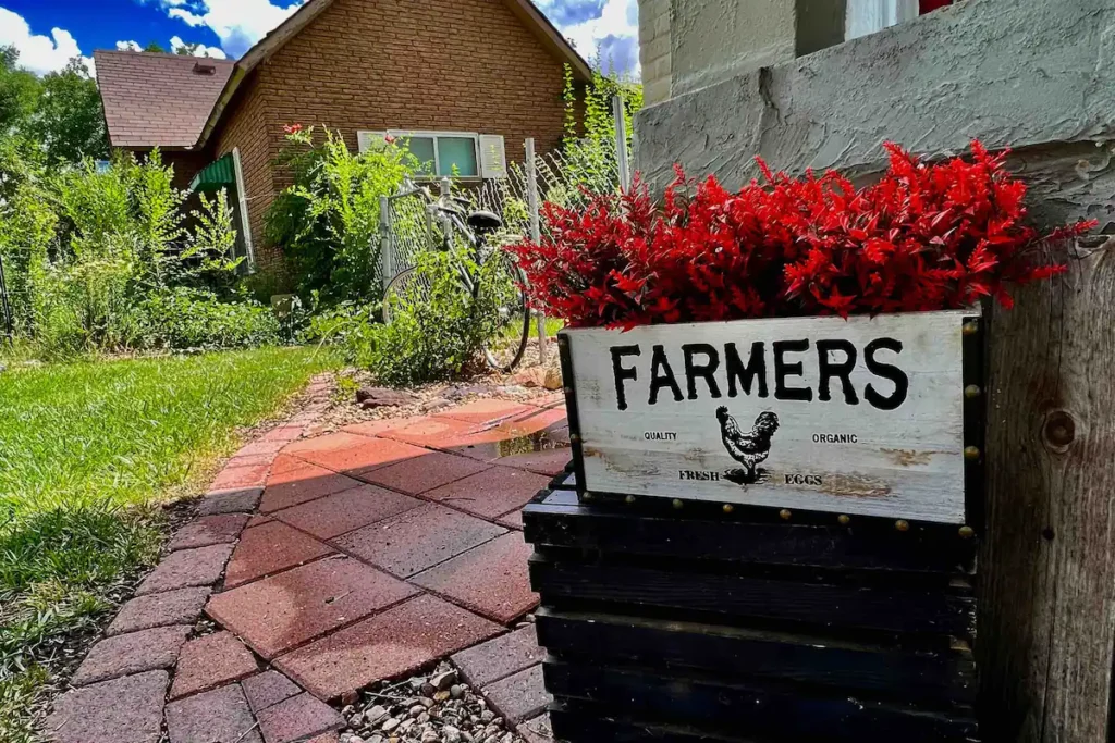 A box of red flowers that says farmers with a house in the background.