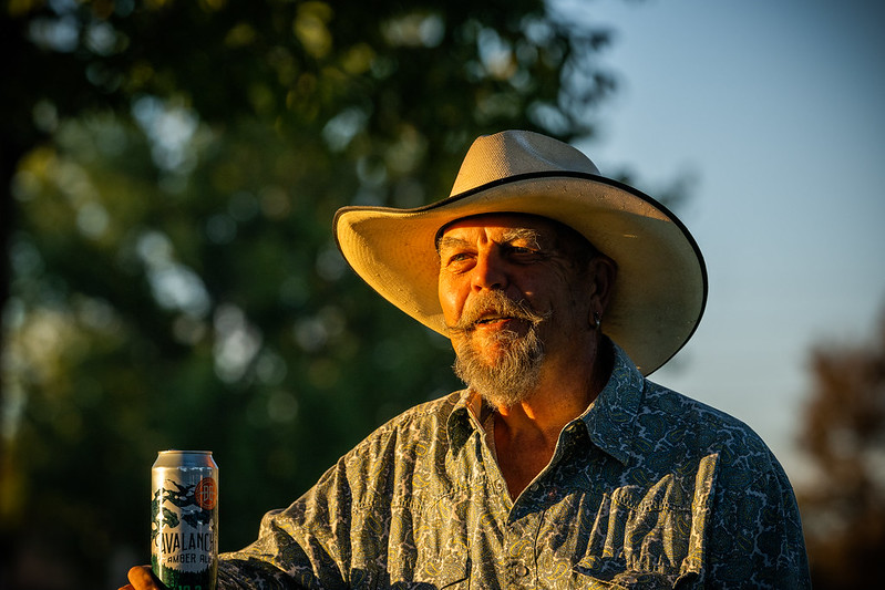 A bearded man with a cowboy hat on drinks an Avalanche Amber Ale.