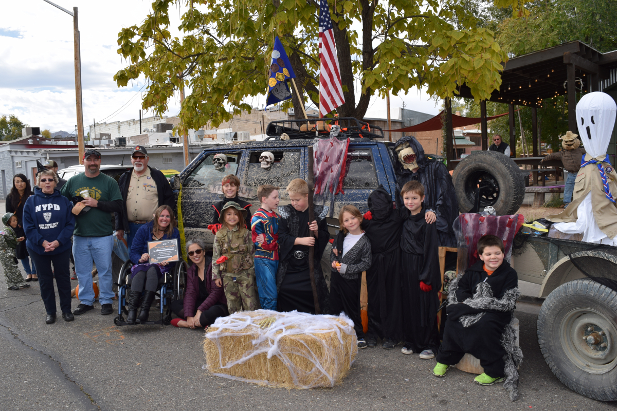 A group of adults and children in Halloween costumes pose in front of a truck.