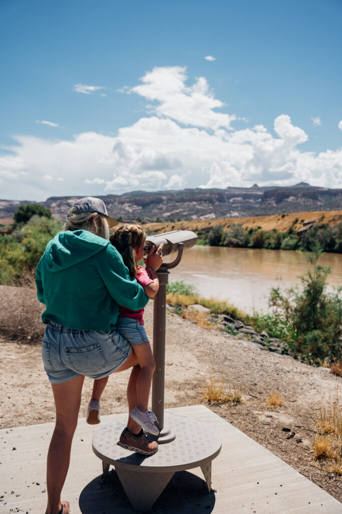 A mom holds her kid up to see into a telescope.