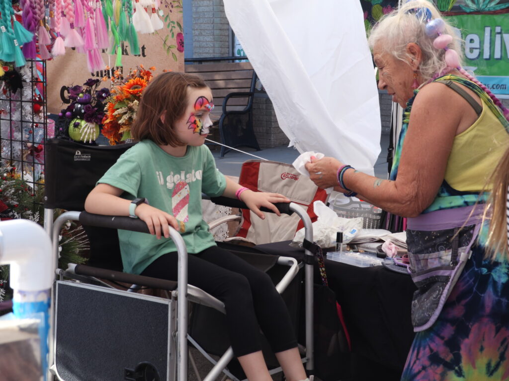 A woman paints a young girl's face to look like a tiger.