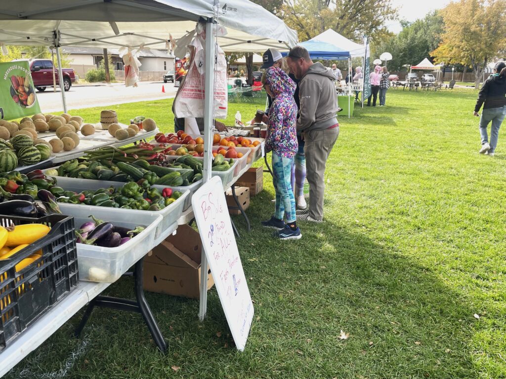 A family of three look at vegetables at a stand at the Fruita Farmers Market.
