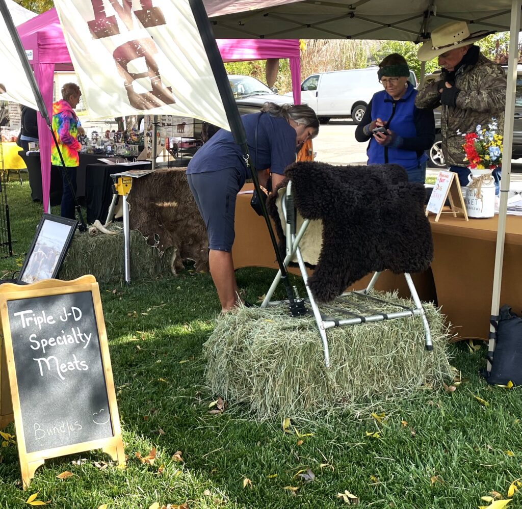 A woman looks at different cuts of meat at a booth at the Fruita Farmers Market.