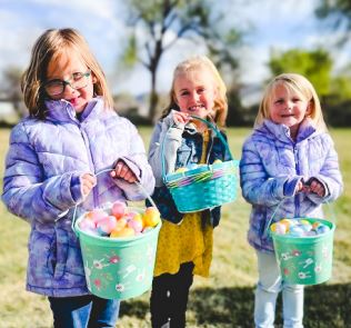 Three little girls hold Easter baskets filled with eggs.