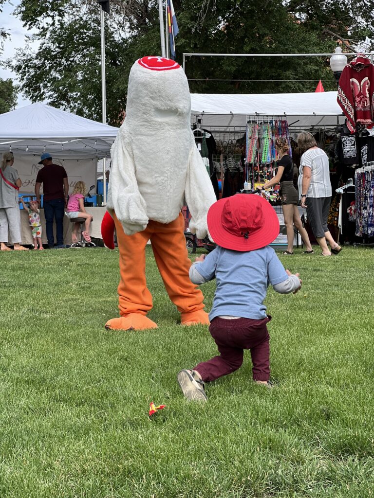 A headless chicken mascot interacts with a young kid.