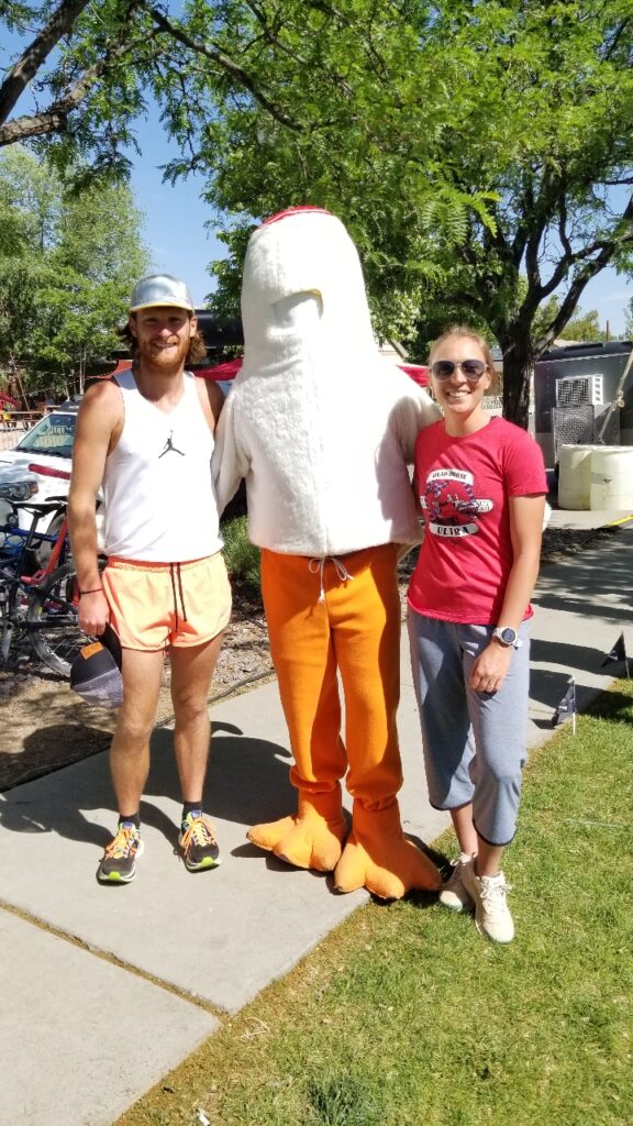 A headless chicken mascot poses with a man and a woman.