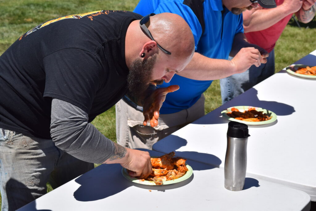 A man with a beard eats a plate of chicken wings during a contest.