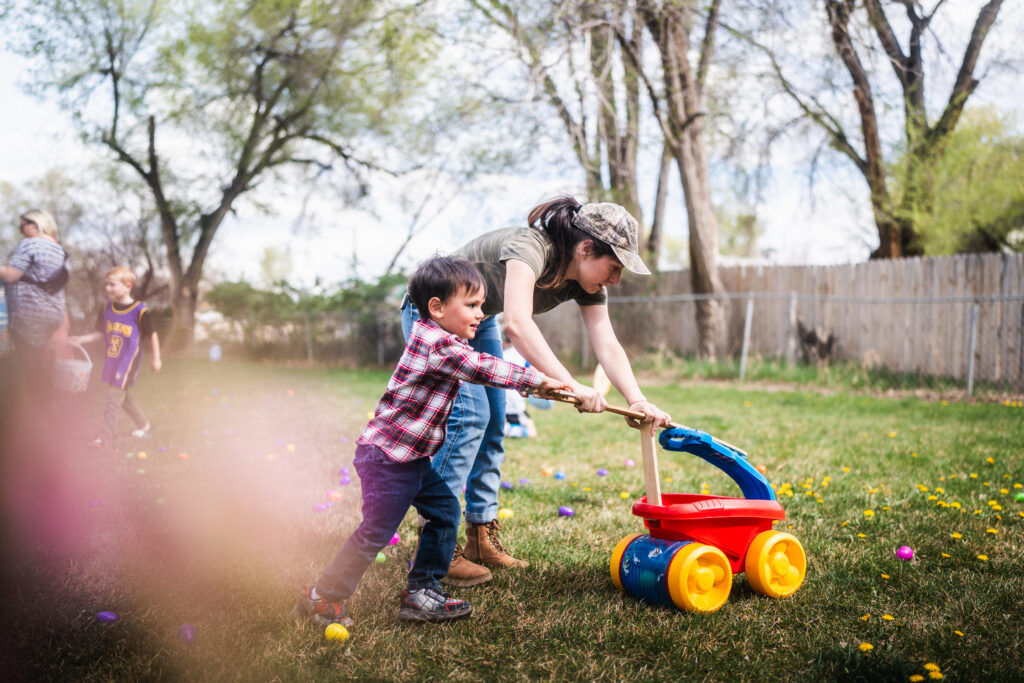 A child and his mother push a cart while collecting easter eggs.