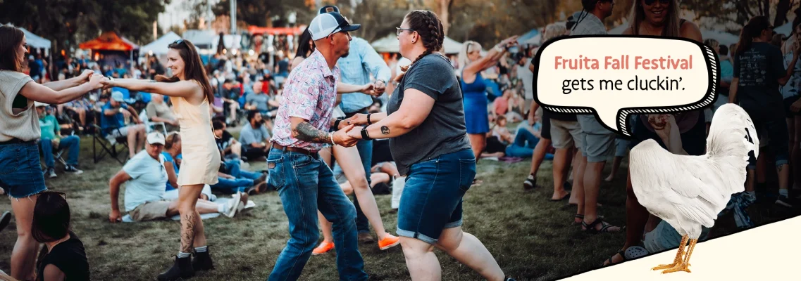 People dance at an outdoor festival with Mike the Headless Chicken in the foreground